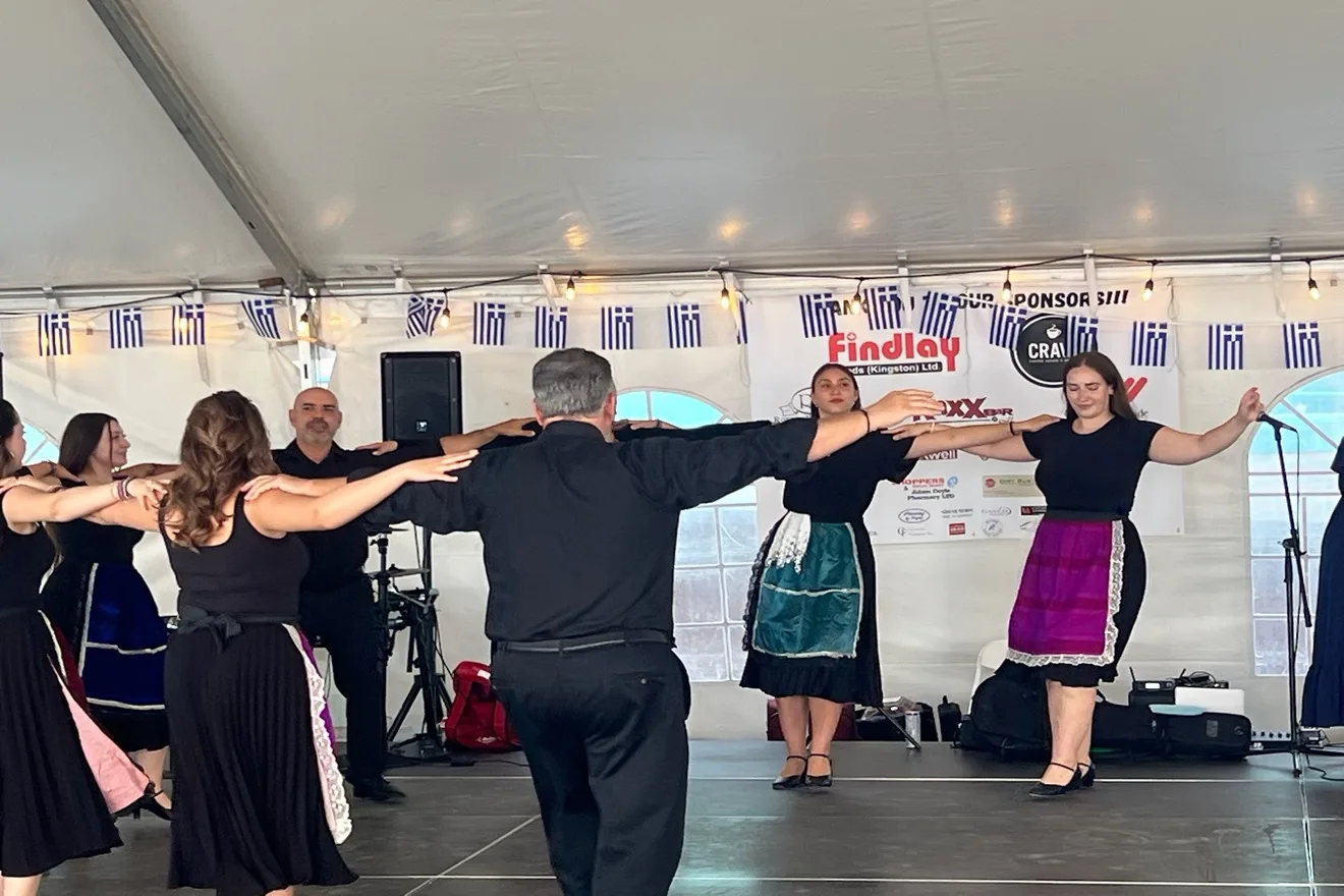 Levendia-X dancers with hands on each other's shoulders in a line dance on the festival stage