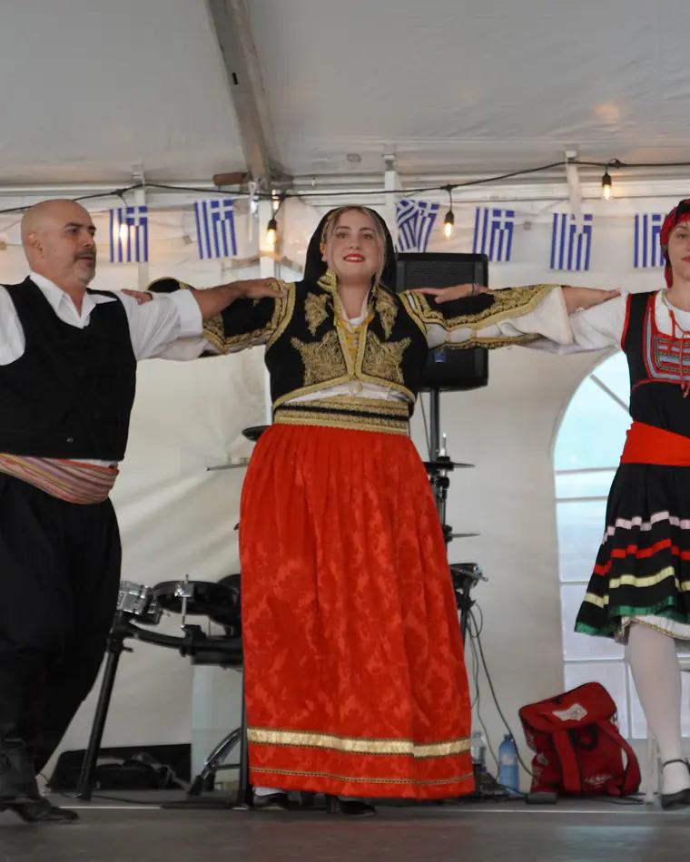 Performers in traditional Greek dress greeting the crowd from the stage